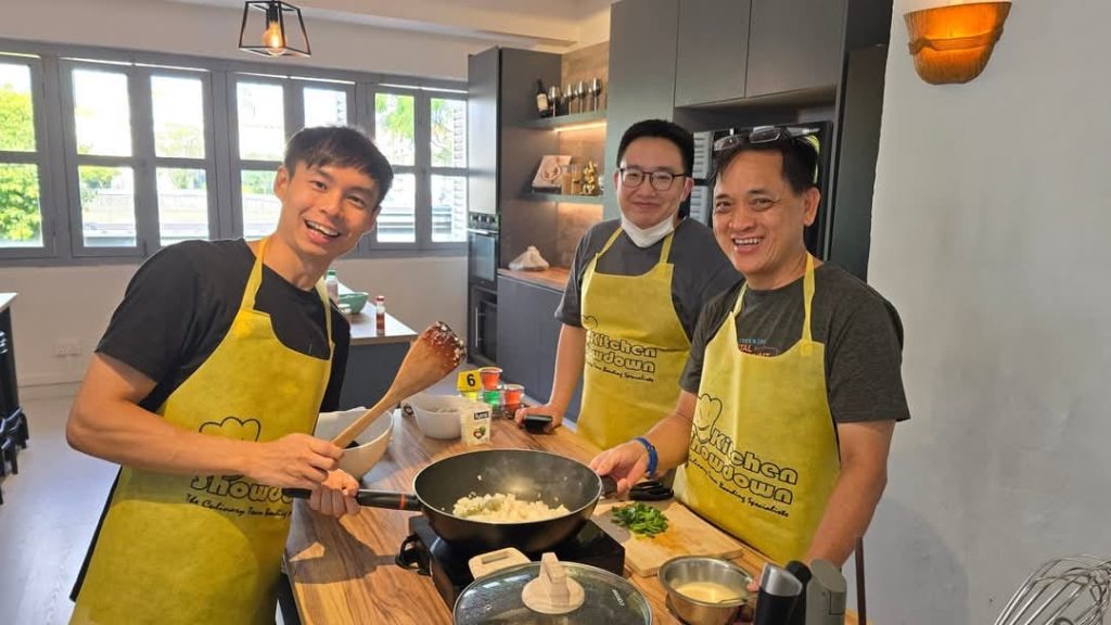 Three men in yellow Kitchen Showdown aprons cooking together at a corporate team building session