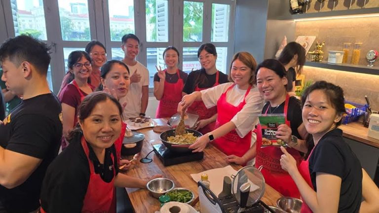 Large group in red Kitchen Showdown aprons cooking a shared dish at a team building class